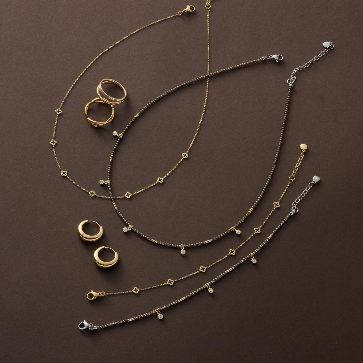 Armband ANNA CIAO in Gold- und Silbertönen mit Ringen und Schmuckstücken auf braunem Untergrund