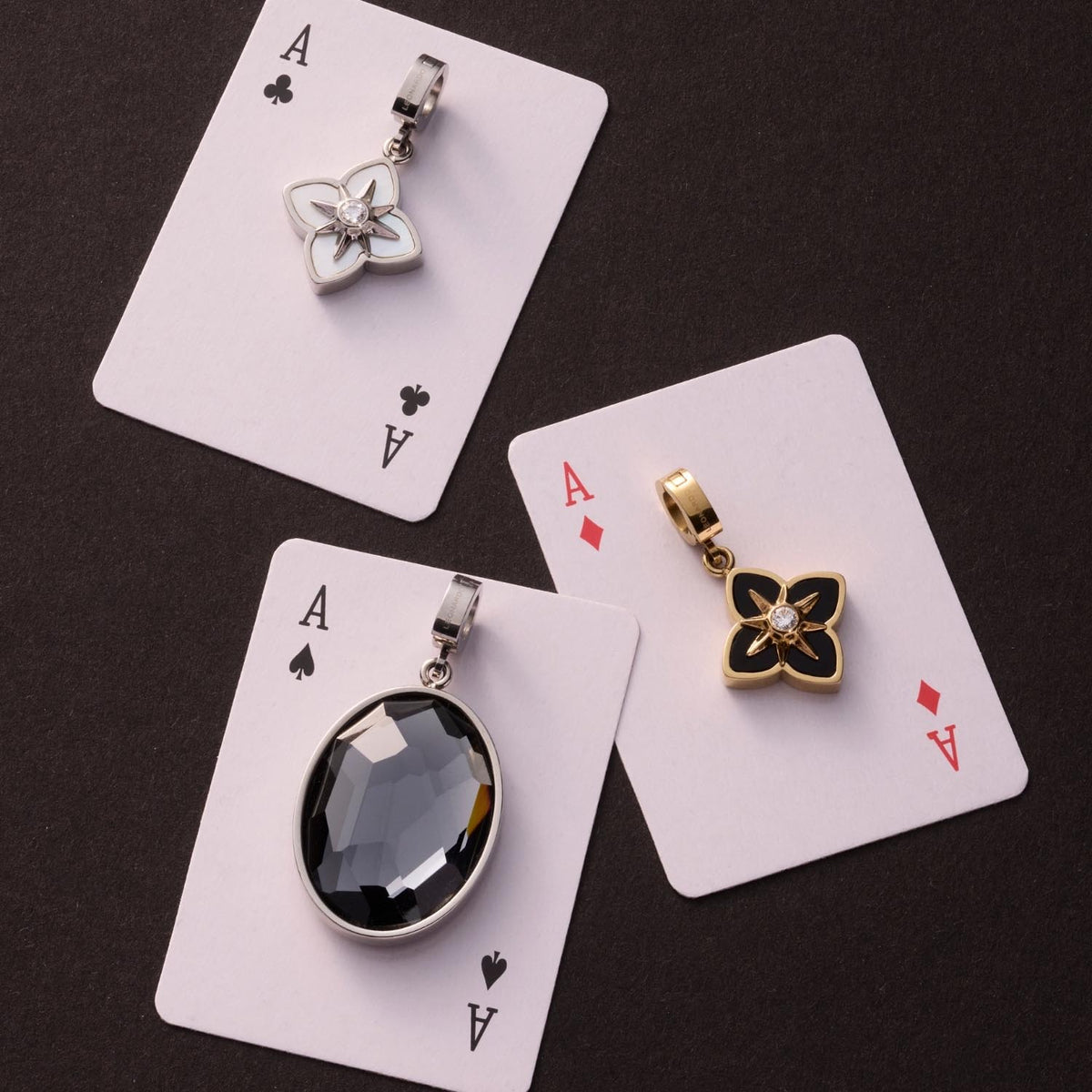 Drei Spielkarten mit silbernen und goldenen Anhängern auf dunklem Untergrund