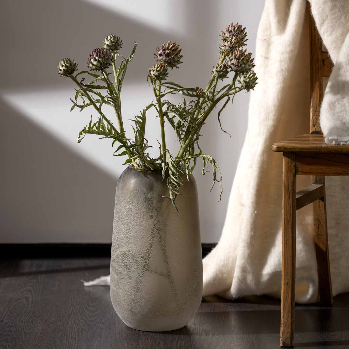 Vase TROGOLO mit getrockneten Blüten in hellem Wohnraum neben Textilien