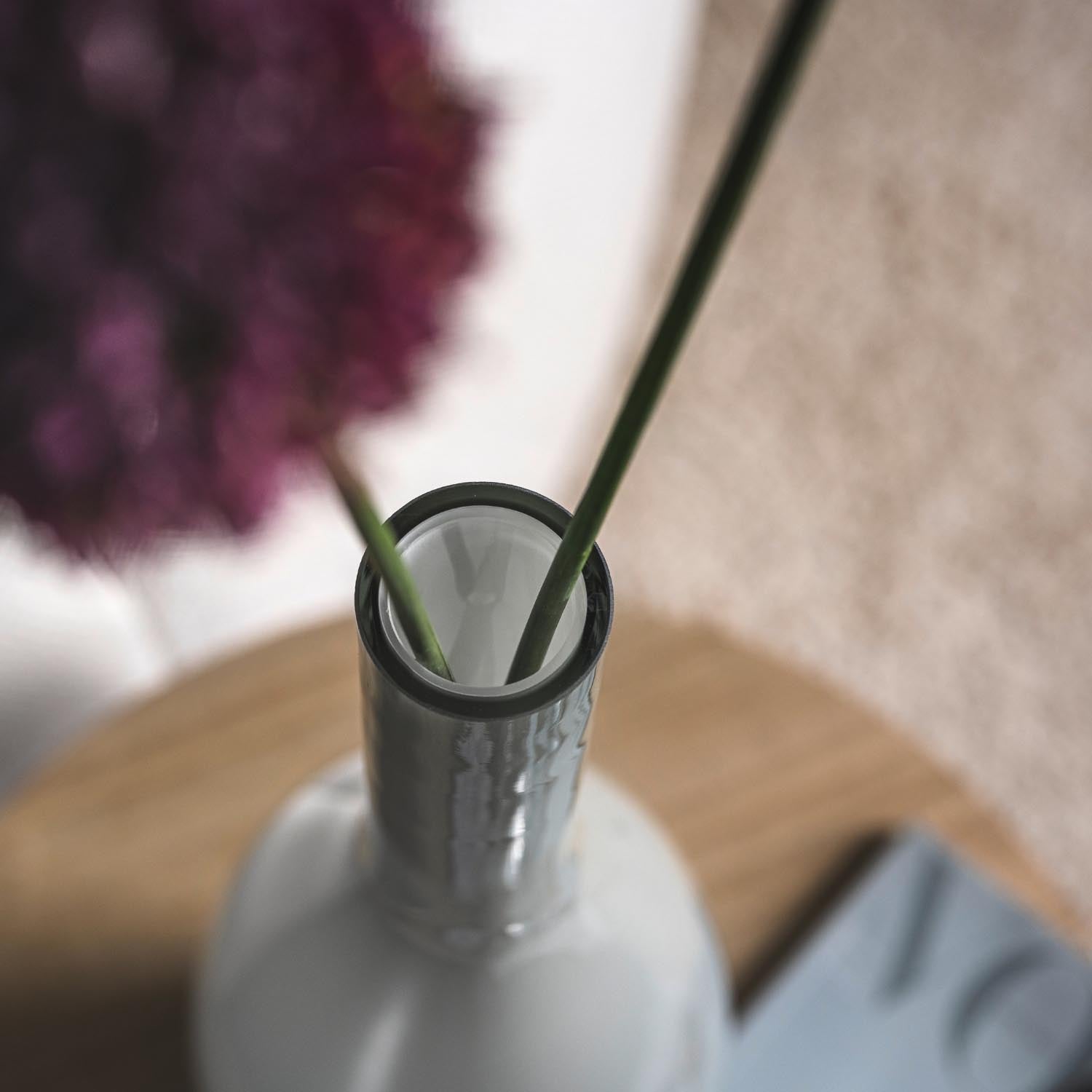 Vase BEAUTY grau mit Blumenstiel und unscharfem Blütenhintergrund auf Holztisch