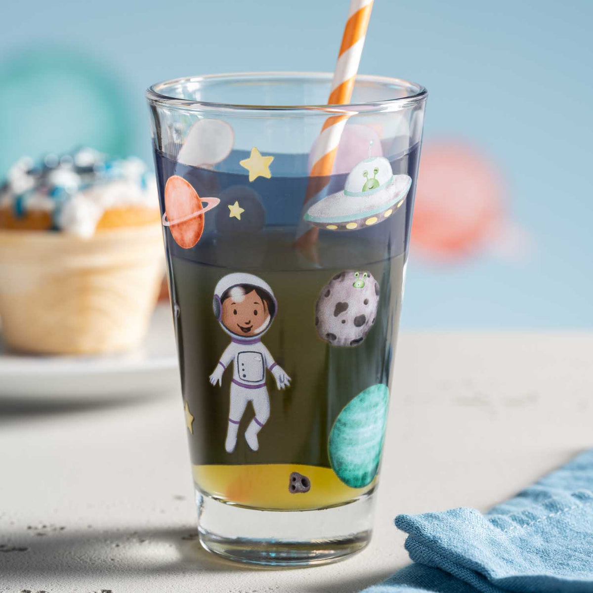 Trinkglas BAMBINI AVVENTURA mit Weltall-Motiven, Strohhalm, auf Tisch mit Deko