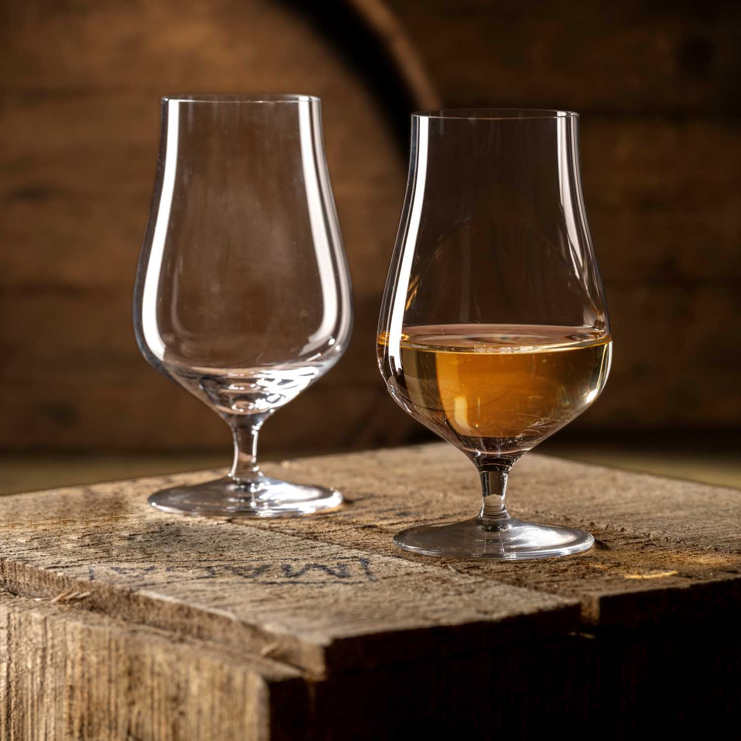 Zwei Whiskygläser BRUNELLI auf Holzoberfläche, eines leer, eines mit bernsteinfarbenem Inhalt