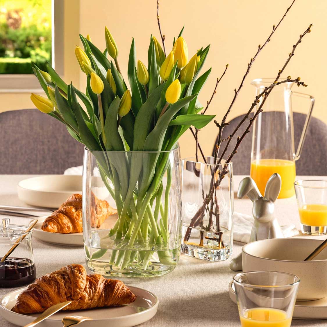 Gedeckter Frühstückstisch mit Tulpen, Croissants, Orangensaft und Tellern