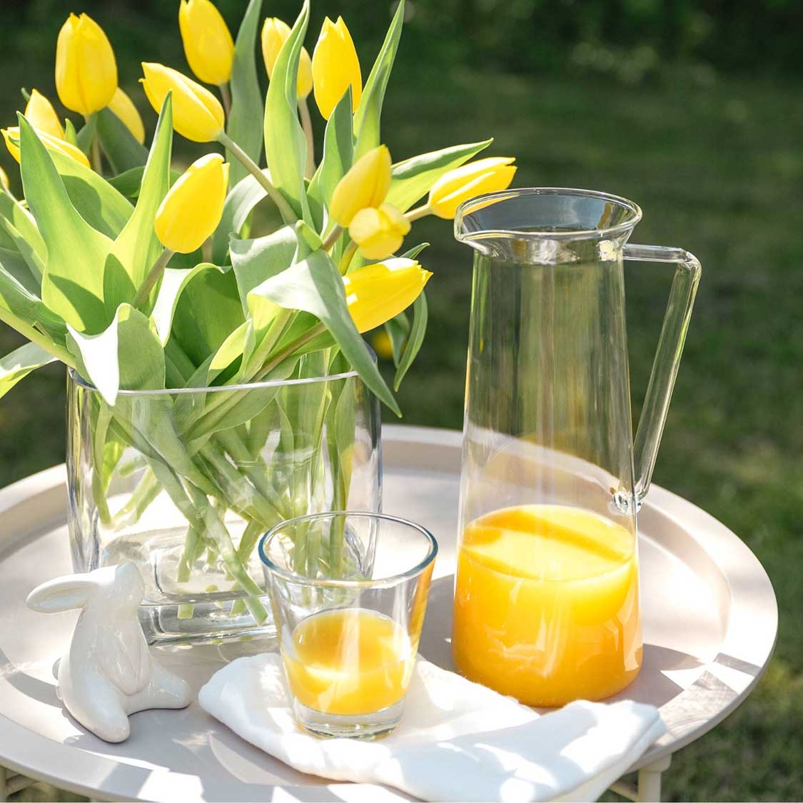 Gelbe Tulpen in Vase auf Tisch mit Orangensaft und Glas im Freien