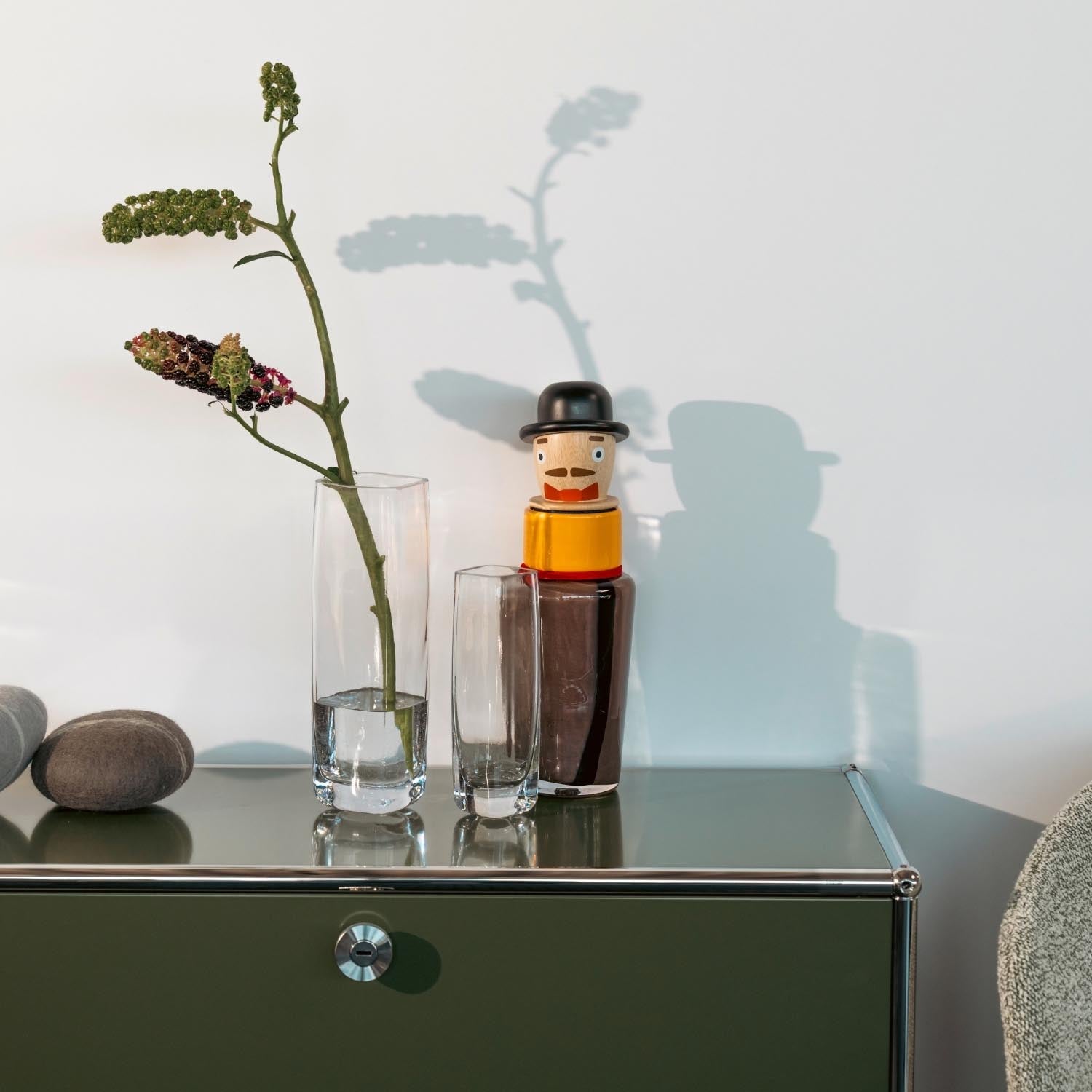 Solifleurvase mit Blumenzweigen auf grünem Sideboard, dekoriert mit Flasche und Steinen