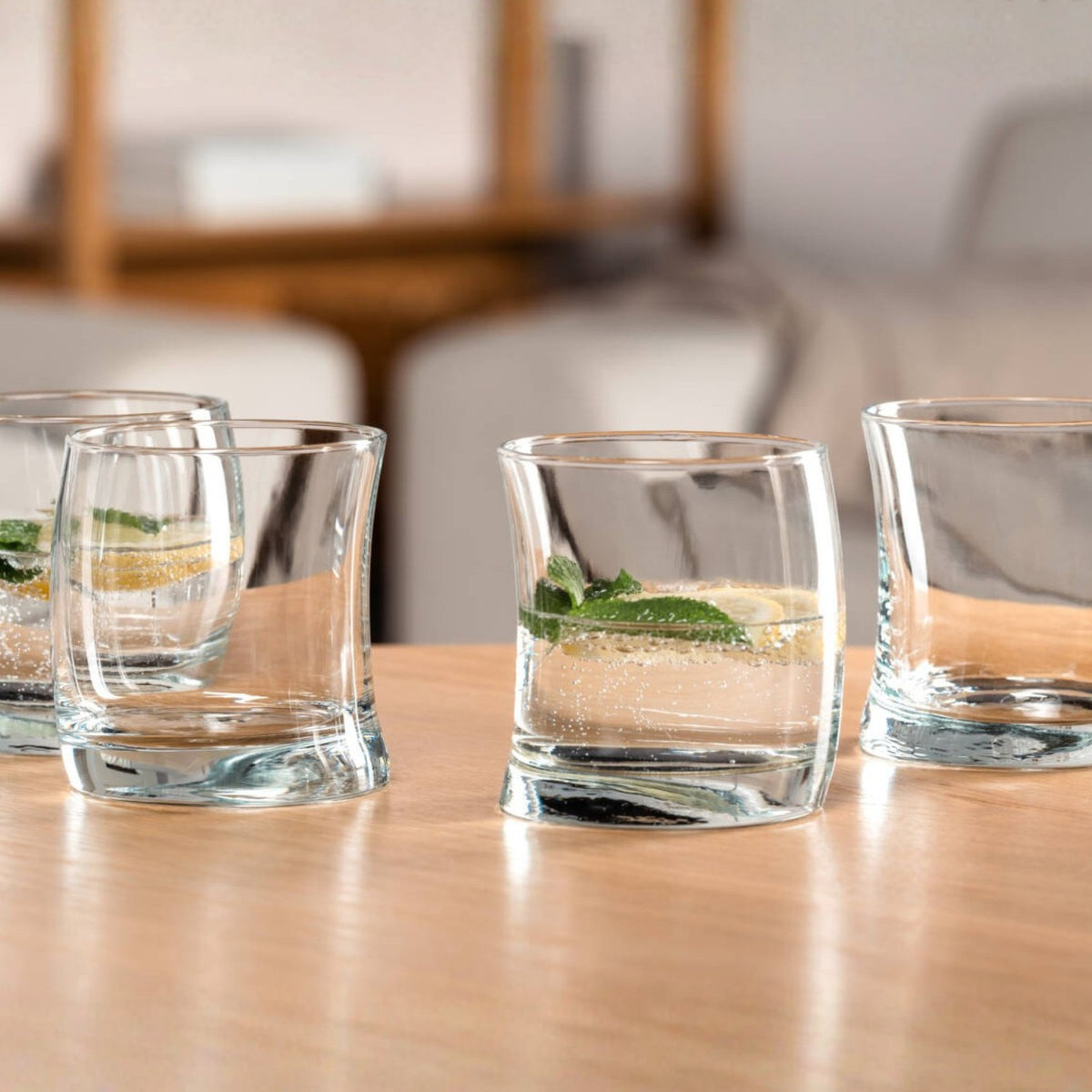 Vier Trinkgläser SWING auf Holztisch, gefüllt mit Wasser und Minze, Wohnraum im Hintergrund