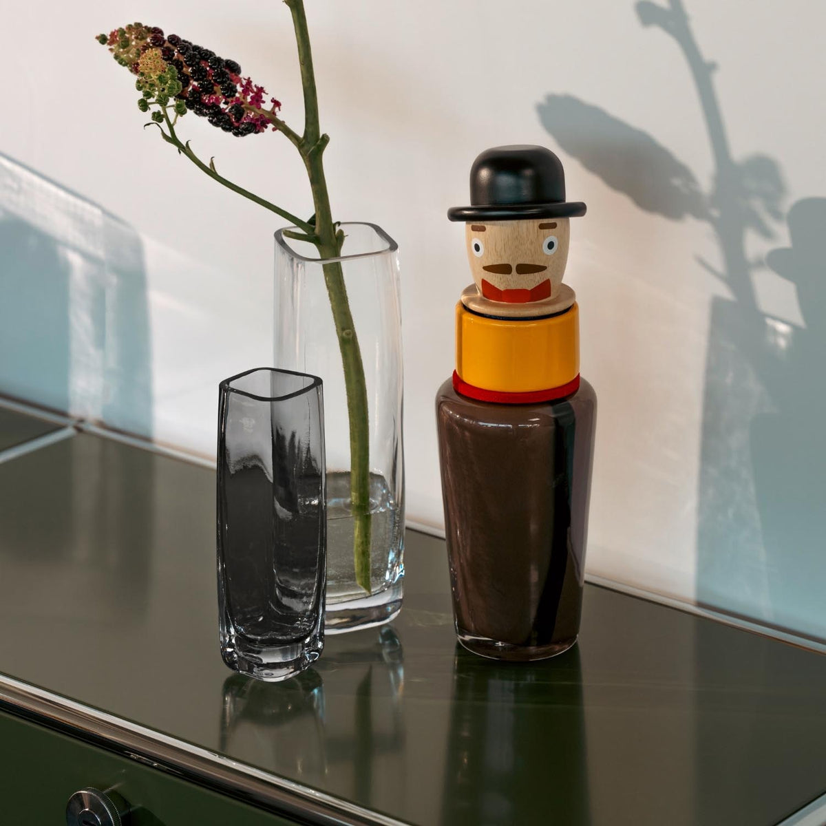 Solifleurvase PIETRA mit Blume, daneben dekorative Holzfigur auf Tisch