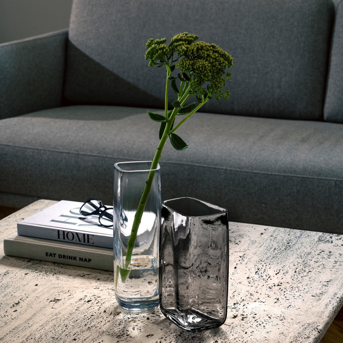 Vase PIETRA mit grünem Kraut auf Wohnzimmertisch neben Büchern und Gläsern