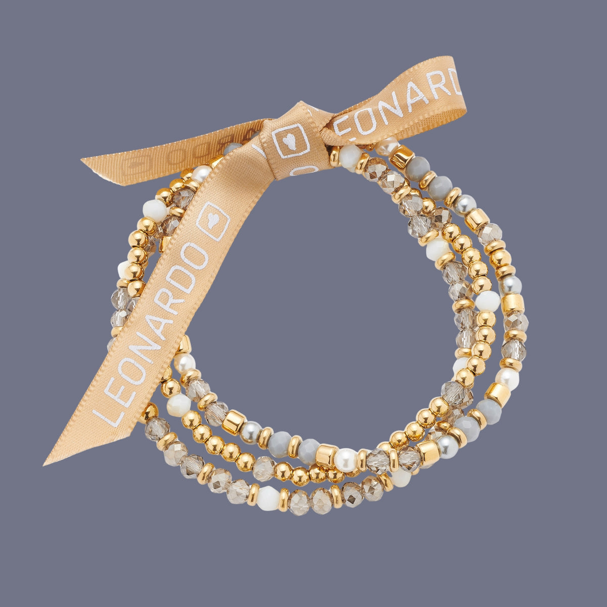 Ein mehrreihiges Armband aus goldfarbenen und schimmernden Perlen, gebunden mit einer beigefarbenen Schleife mit LEONARDO-Logo auf violettem Hintergrund.