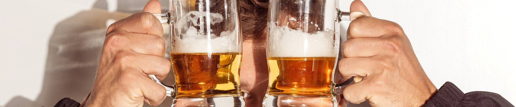 Zwei Männerhände stoßen mit gefüllten Biergläsern an, warme braune Farbstimmung, weißer Hintergrund