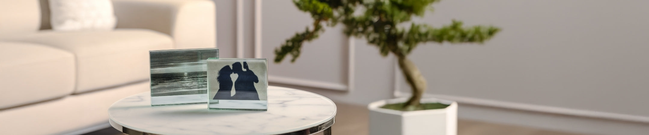 Moderne Wohnzimmerecke mit weißem Couchtisch, darauf arrangierte Bilderrahmen und eine Bonsai-Pflanze, helles Interieur