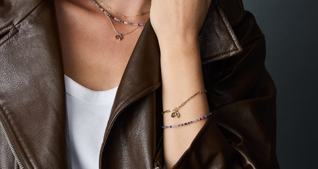 Frau trägt braune Lederjacke, silberne Halskette mit Anhänger und zwei feine Armbänder in Gold und Blau