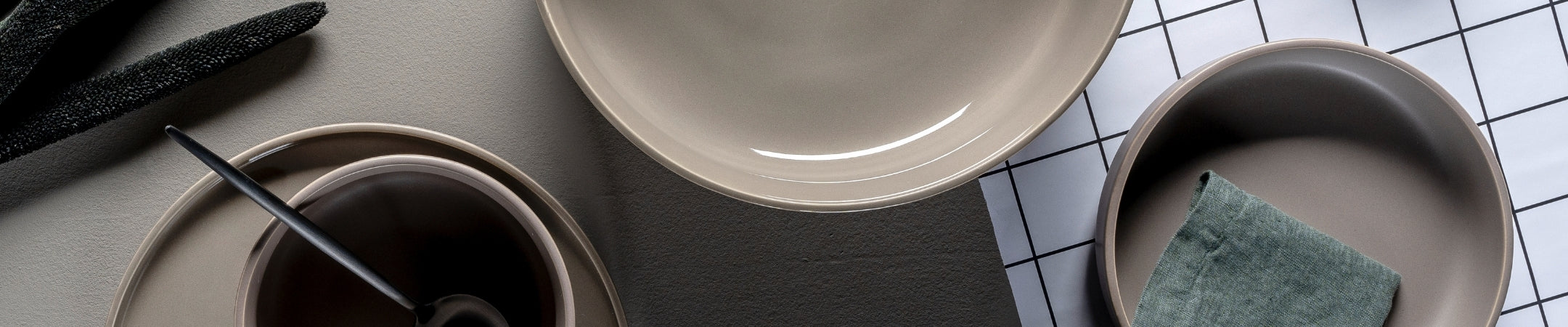 Minimalistisch angeordnete Keramikschüsseln und -teller in Grau- und Beigetönen mit Besteck auf strukturiertem Hintergrund