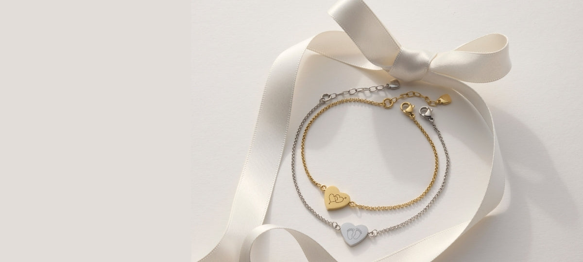 Zwei goldene Armbänder mit herzförmigen Anhängern auf weißem Seidenband, elegante Geschenkpräsentation