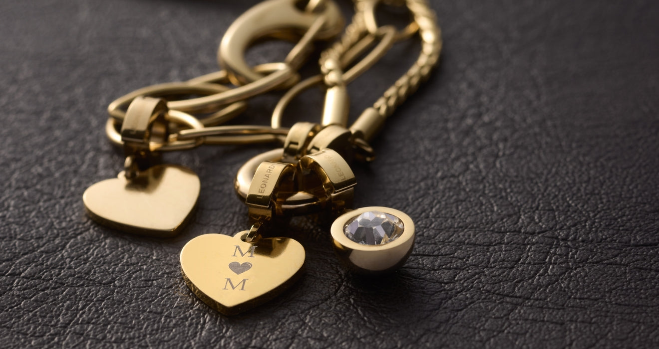 Goldenes Armband mit gravierten Herz-Anhängern und Kristall-Schmuckstein auf dunklem Untergrund