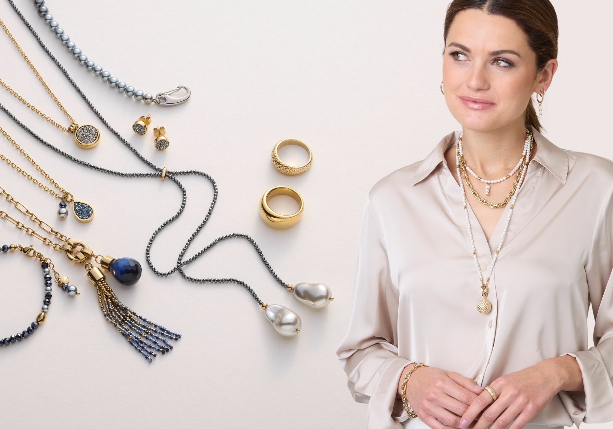 Elegante Frau trägt mehrere übereinander geschichtete Perlen- und Gliederketten in Gold – daneben eine Auswahl an passenden Ringen, Ketten und Armbändern auf hellem Untergrund.