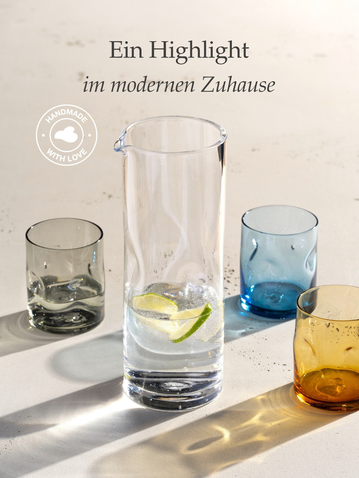 Schlanke Glaskaraffe mit Limettenscheiben in sprudelndem Wasser, umgeben von vier farbigen Trinkgläsern in Blau, Gelb und Braun, im Sonnenlicht inszeniert. "Ein Highlight im modernen Zuhause"