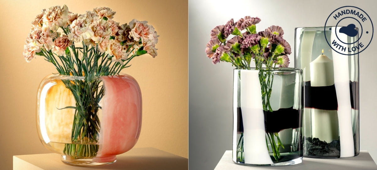 Zwei handgefertigte Glasvasen mit floraler Dekoration: Links eine rundliche Vase mit zarten Nelken in einer warmen Farbkombination aus Gelb und Rosé, rechts zwei zylindrische Vasen in klarem Glas mit kunstvollen weißen und schwarzen Farbverläufen – eine davon mit violetten Nelken, die andere mit einer Kerze. Oben rechts befindet sich das Siegel „Handmade with Love“, das auf liebevolle Handarbeit hinweist.