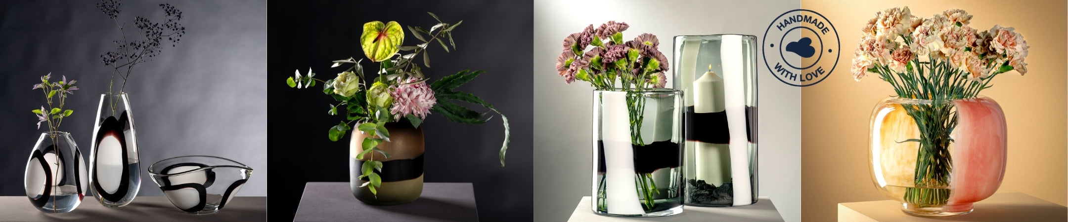 Eine stilvolle Komposition handgefertigter Glasobjekte mit unterschiedlichen Formen und Dekoren: Links organisch geformte Vasen und eine Schale mit schwarzer und weißer Musterung, in der Mitte eine goldfarbene Vase mit kunstvollem Blumenarrangement, daneben zwei zylindrische Vasen mit schwarzen und weißen Farbstreifen – eine davon mit violetten Nelken, die andere mit einer Kerze. Ganz rechts eine rundliche Vase mit orange-rosafarbenem Verlauf und pastelligen Nelken. Das Qualitätssiegel „Handmade with Love“ 