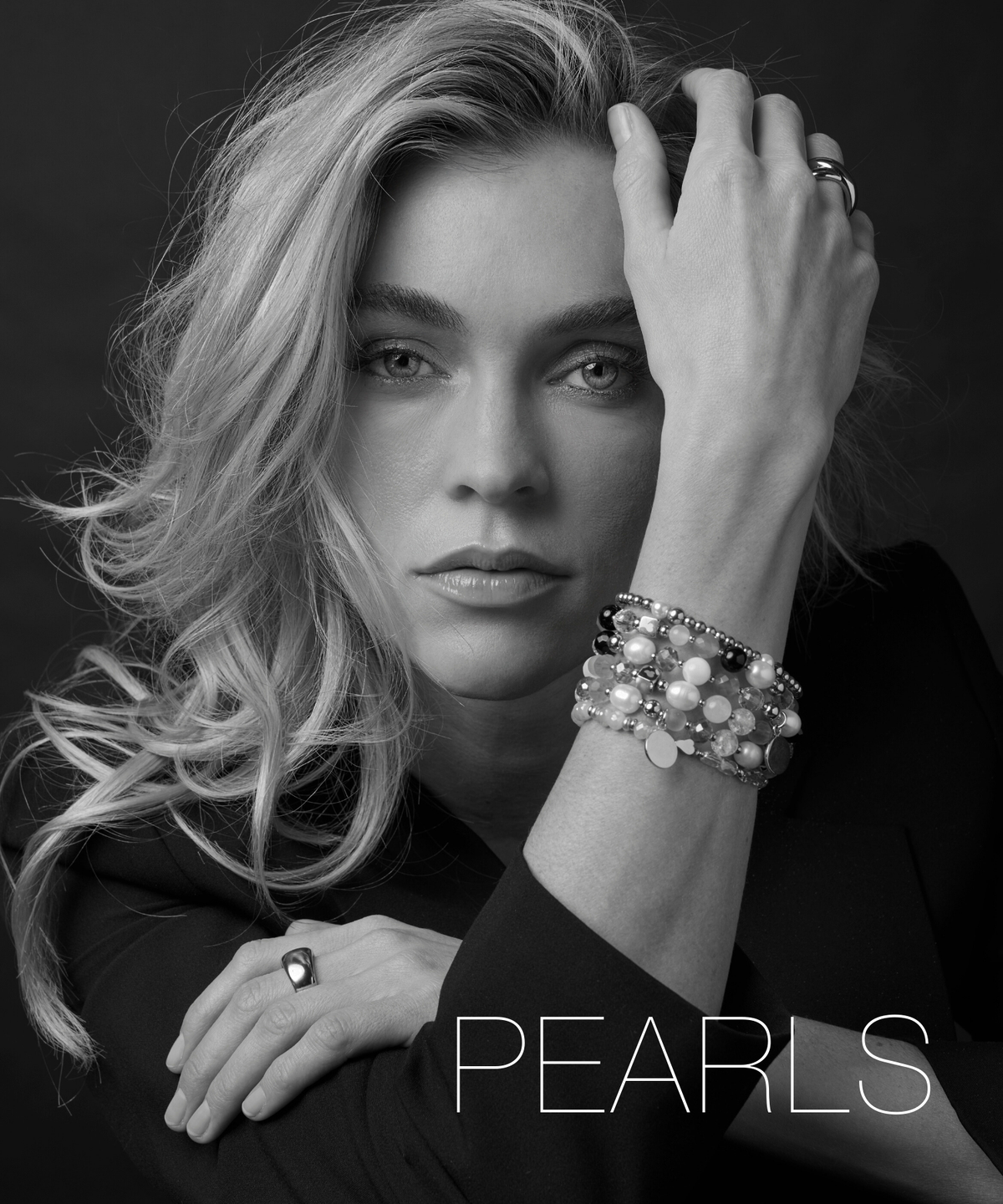 Schwarz-weiß-Foto einer Frau am Strand mit mehreren Ketten und Anhängern. Sie steht mit Händen in der Hüfte. Schriftzug ‚Casual‘ im Bild.