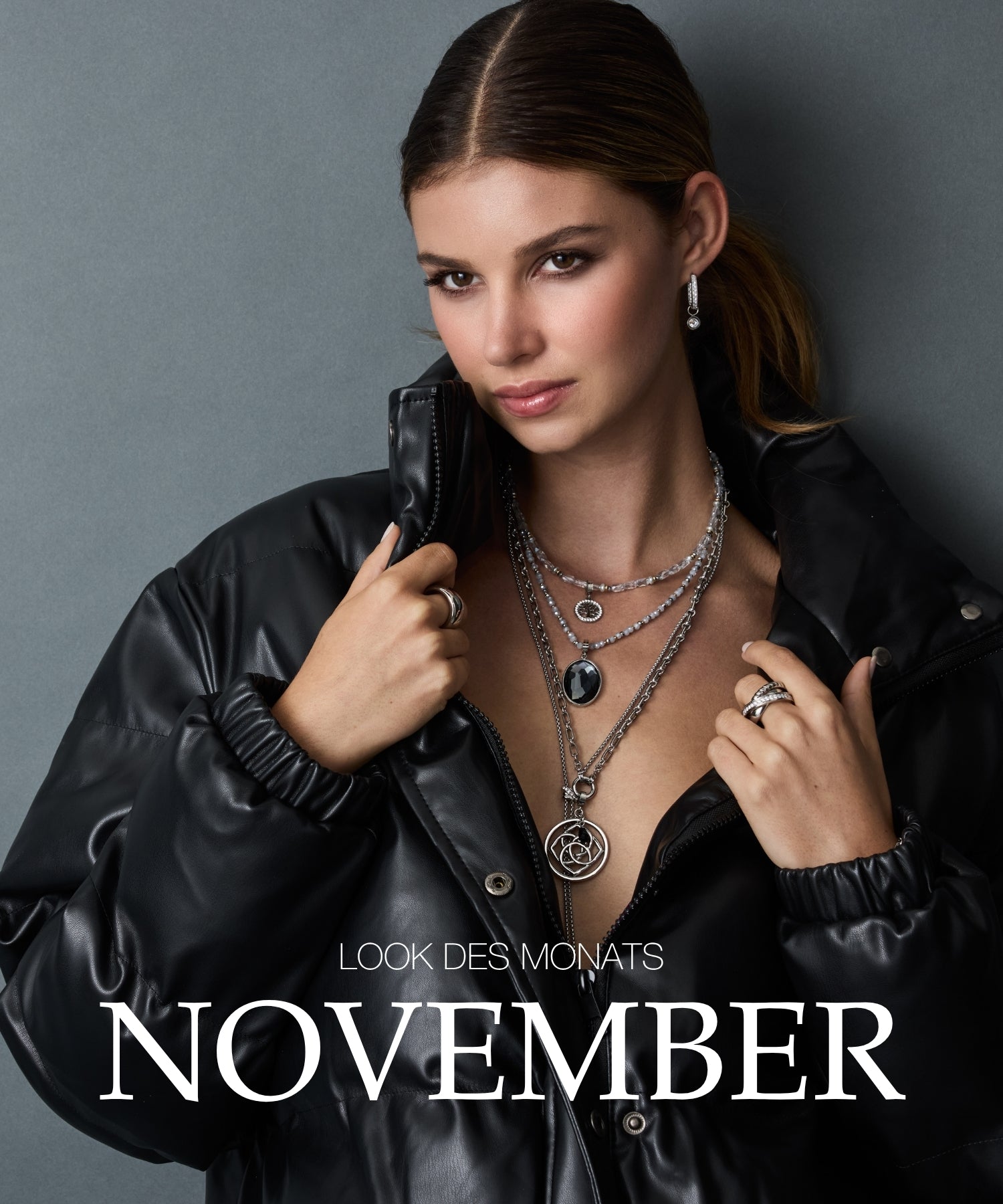 Look des Monats November: Frau mit schwarzer Lederjacke und mehrlagiger Silberkette mit Anhängern vor grauem Hintergrund