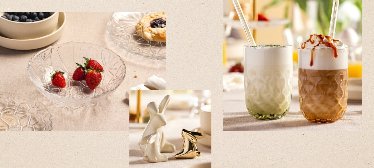 Gläserne Dessertschalen mit Erdbeeren und Gebäck auf hellem Tisch sowie zwei cremige Heißgetränke mit Glasstrohhalmen und kleine Hasen-Dekofiguren.