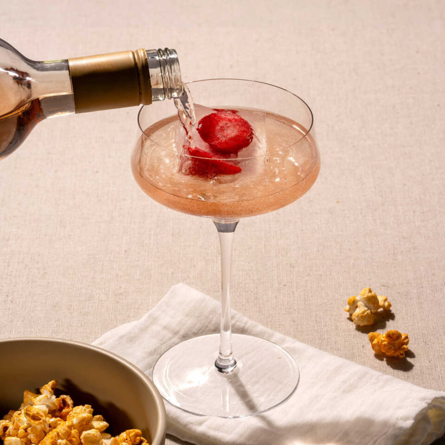 Ein prickelndes Getränk mit gefrorenen Erdbeeren wird in eine elegante Champagnerschale gegossen – daneben steht eine Schale mit süßem Popcorn.