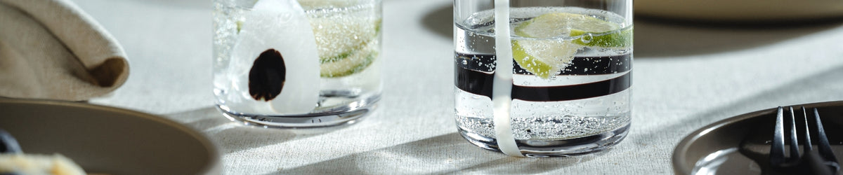 Elegante Gläser mit Wasser, Limette und Oliven auf hellem Leinen neben Besteck und Serviette
