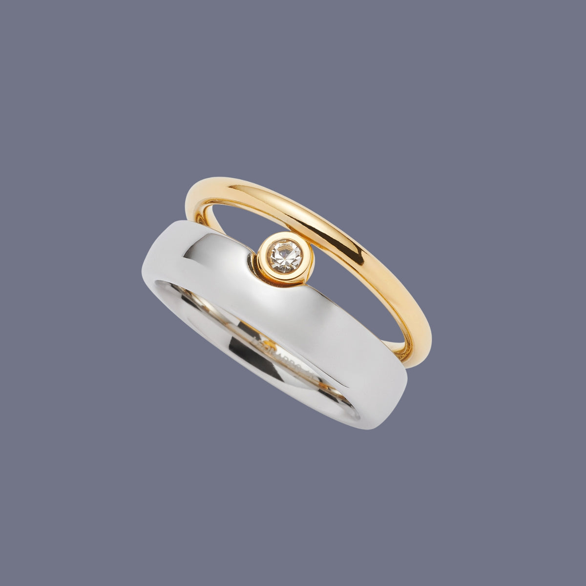 Zwei elegante Ringe, einer in Gold mit Zirkonia, der andere in glänzendem Silber, übereinandergelegt auf grauviolettem Hintergrund.