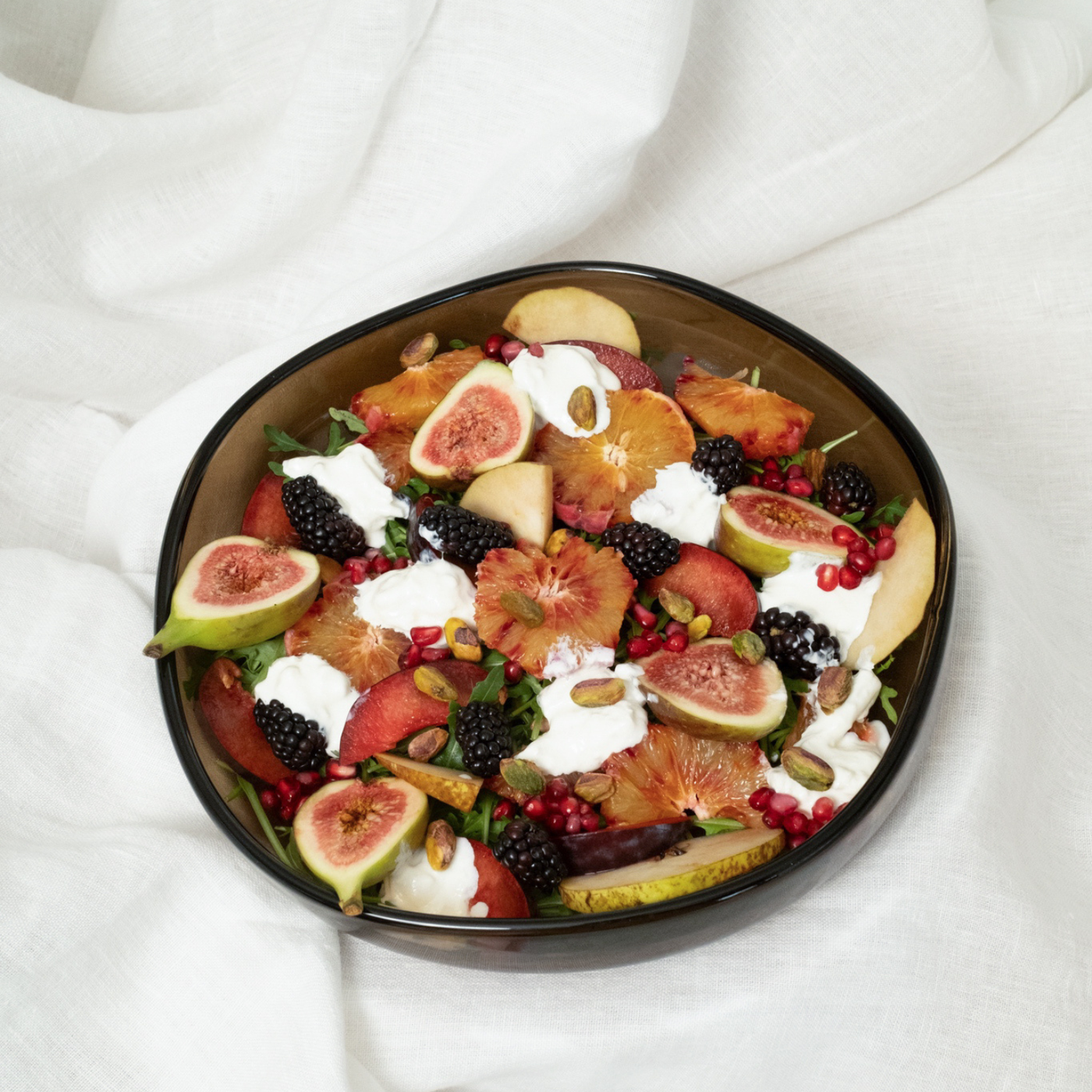 Dunkle Glasschale gefüllt mit Salat aus Feigen, Orangen, Brombeeren, Granatapfelkernen und Joghurt.