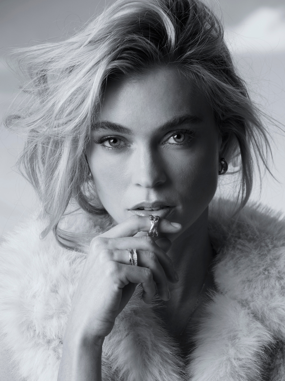 Schwarz-weiß-Porträt einer Frau mit kurzem blondem Haar, die mehrere Ringe trägt und direkt in die Kamera blickt.