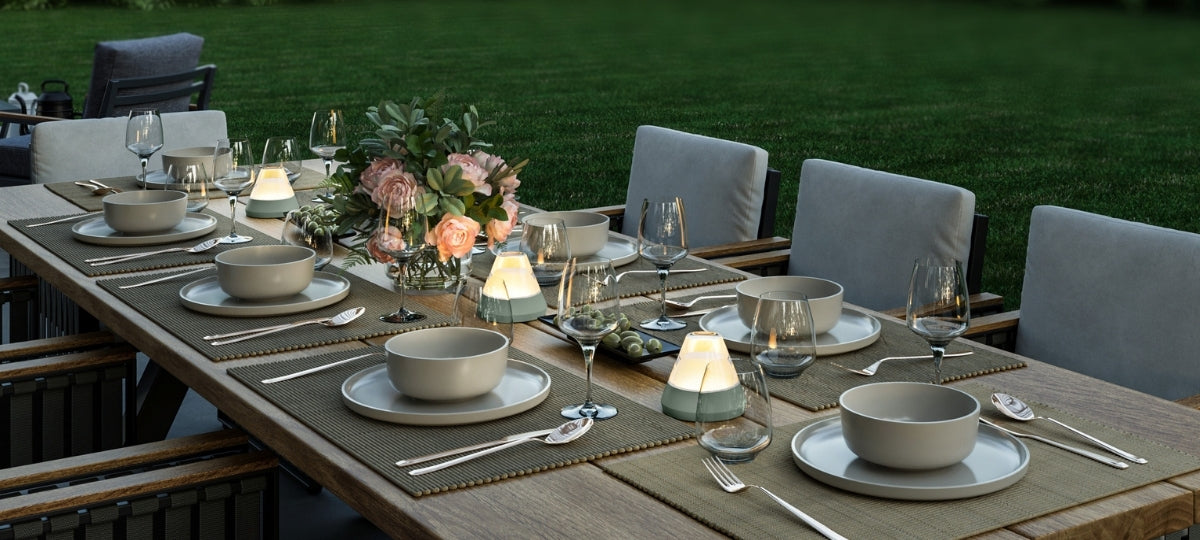 Elegant gedeckter Gartentisch mit LEONARDO Geschirr, Weingläsern, LED-Leuchten und Blumendekoration bei Abendstimmung.