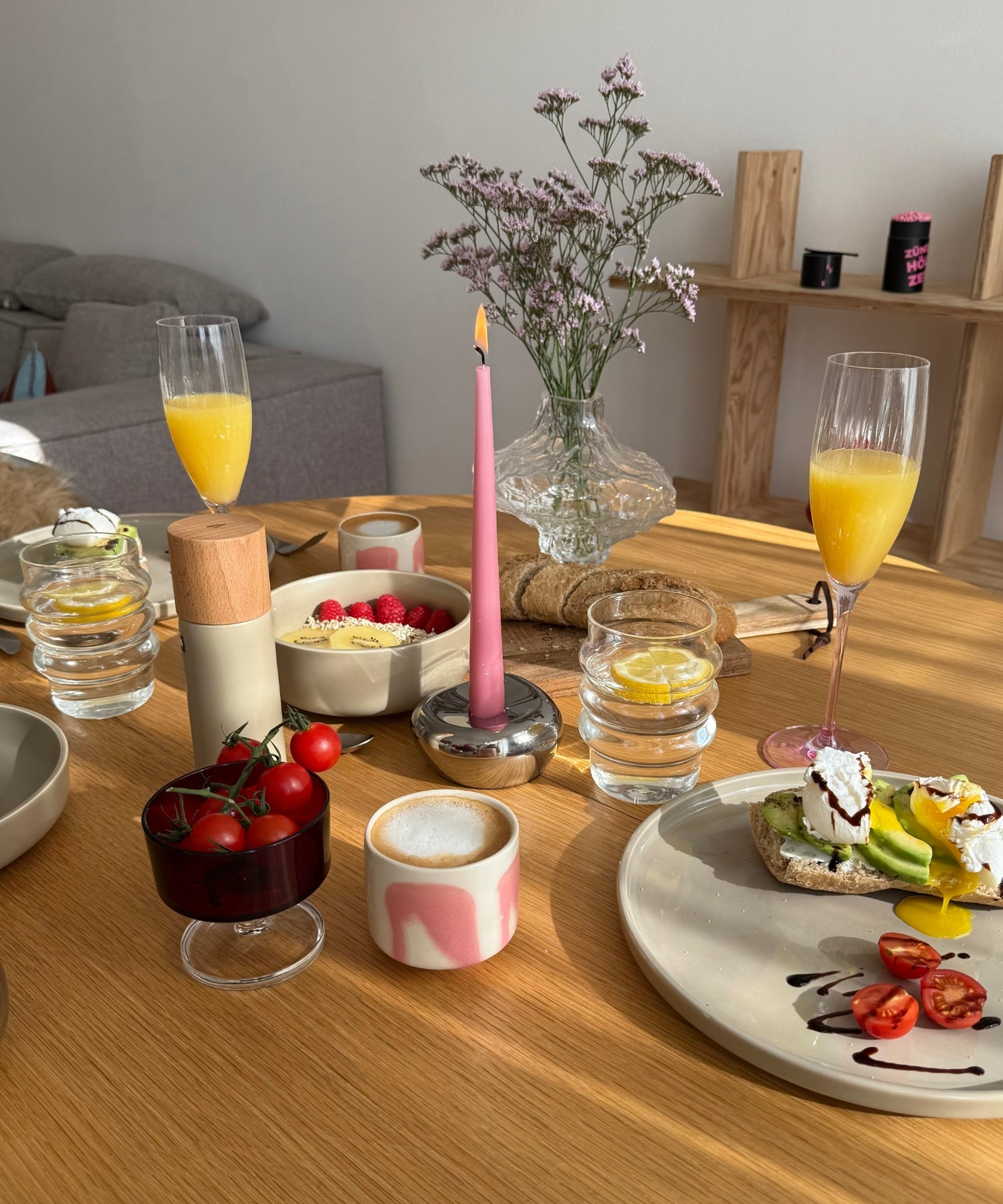 Modern gedeckter Frühstückstisch mit Zitronenwasser, Avocado-Toast, Beeren und Kerze in zarten Rosétönen für einen sonnigen Start in den Tag.