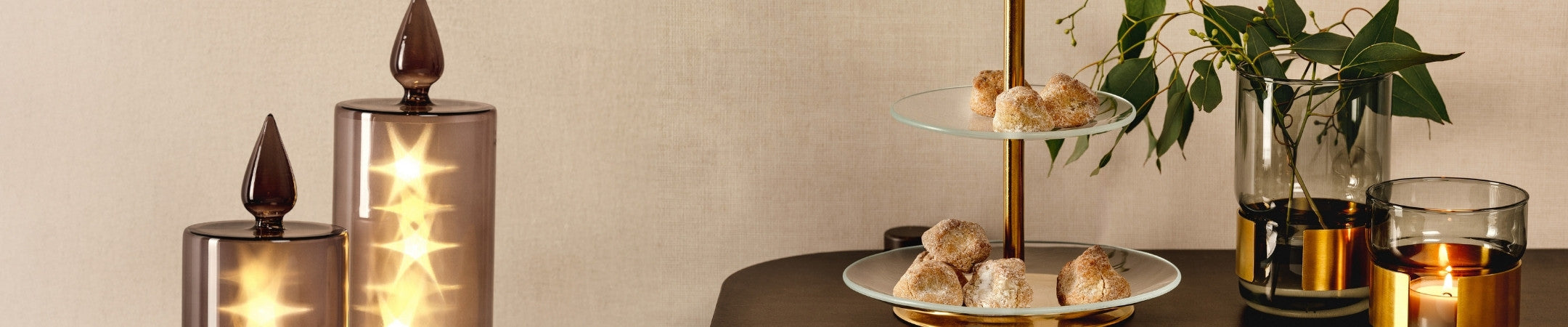 Breiter Weihnachtsbanner mit goldener Etagere voller Gebäck, dekorativen Glasvasen und Kerzen im stimmungsvollen Ambiente.